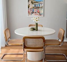 a white table with four chairs around it and a vase filled with flowers on top