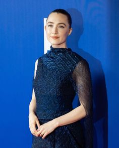 a woman standing in front of a blue wall wearing a black dress with sheer sleeves