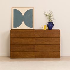 a wooden dresser sitting next to a blue vase on top of a white wall in a room