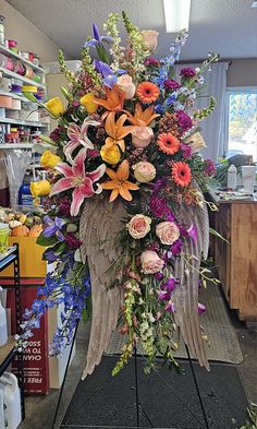 an arrangement of flowers and angel wings in a shop display case with other items on the shelves