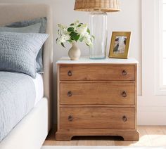 a wooden dresser sitting next to a bed in a room with a lamp on top of it