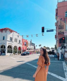 a woman in an orange dress is standing on the street and looking up at a traffic light