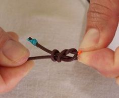 two hands holding a piece of brown string with blue and orange wires attached to it