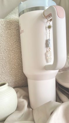 a white cup sitting on top of a bed next to a vase