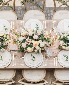 the table is set with white plates and silverware, pink flowers and greenery