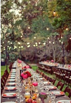 a long table is set with place settings and flowers on it for an outdoor dinner