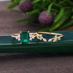 an emerald and diamond ring sitting on top of a green piece of wood next to flowers