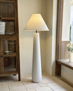 a large white vase sitting on top of a floor next to a lamp and book shelf