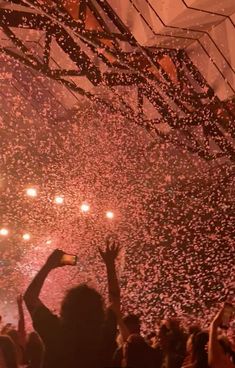 a crowd at a concert with confetti falling from the ceiling and people holding up cell phones