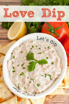 a white bowl filled with dip surrounded by crackers and tomatoes