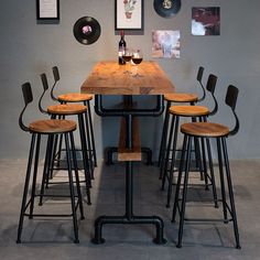 a wooden table with four stools and a wine glass on the top, in front of a gray wall