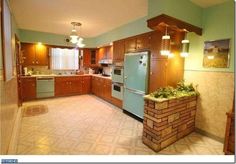 a kitchen with green walls and wooden cabinets, an island in the middle is surrounded by potted plants