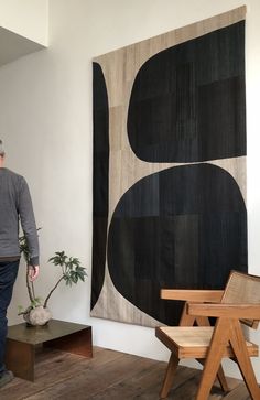 a man standing in front of a large black and white painting next to a wooden chair