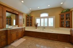 a large bathroom with wooden cabinets and marble counter tops, along with a white bathtub