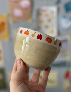 a hand holding a small bowl in front of a wall with pictures on the walls