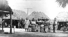 an old black and white photo of some people standing in front of thatched huts