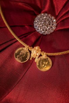 a gold necklace with two medallions attached to it on a red satin cloth background