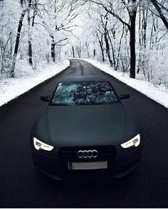 a black car parked on the side of a road in front of snow covered trees