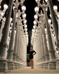 a woman is standing in the middle of a row of white street lamps at night