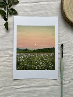 a photo of a field with flowers and a paintbrush on the table next to it