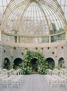 an indoor wedding venue with white chairs and greenery