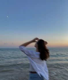 a woman standing on top of a beach next to the ocean under a blue sky