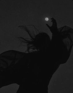 the silhouette of a woman with her hair blowing in the wind, against a dark background