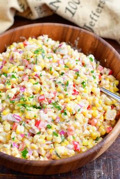 a wooden bowl filled with corn salad on top of a table