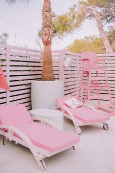 two pink lounge chairs sitting on top of a white tile floor next to a palm tree