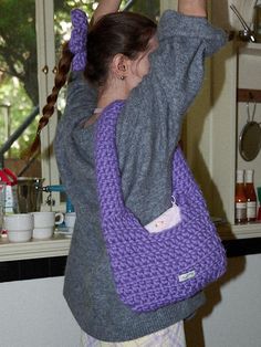 a woman holding onto a purple crocheted purse in the kitchen with her hands up