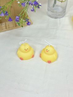 two yellow rubber ducks sitting on top of a white table cloth next to purple flowers