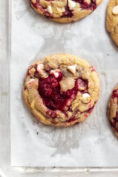 several cookies with white chocolate chips and cherries are on a baking sheet, ready to be baked