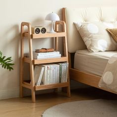 a book shelf next to a bed in a room with white walls and wooden floors