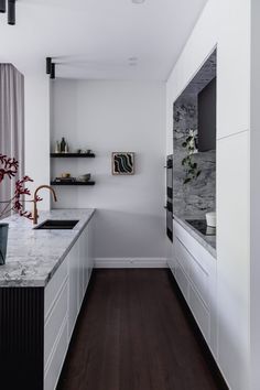 a long narrow kitchen with white cabinets and marble counter tops, along with dark wood flooring