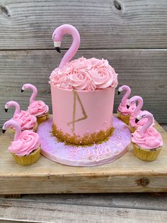 a pink flamingo cake with cupcakes on a wooden table next to it