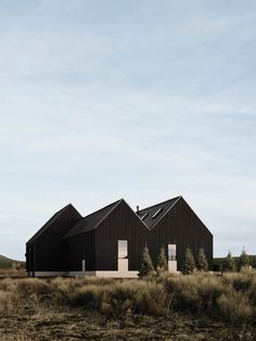 two black buildings sitting on top of a dry grass covered field next to tall trees