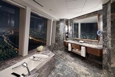 a large bathroom with marble walls and flooring is shown in this image, there are two sinks on the opposite side of the bathtub