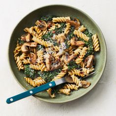 a green bowl filled with pasta, mushrooms and parmesan cheese next to a blue fork