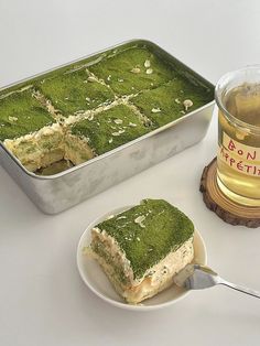 a green cake sitting on top of a white plate next to a container of tea