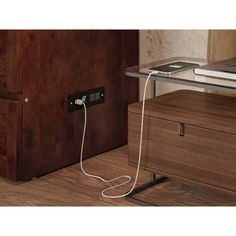 an electronic device is plugged in to a wooden desk with a laptop on it