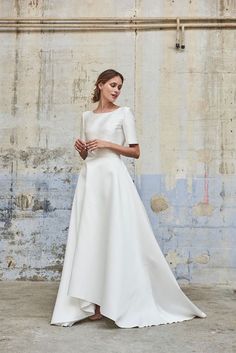 a woman in a white wedding dress standing against a wall with her hands on her hips