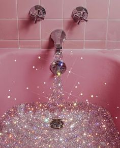 a pink bathtub filled with lots of shiny beads and water running from the faucet