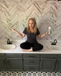 a woman sitting on top of two sinks in a bathroom with black and white tile