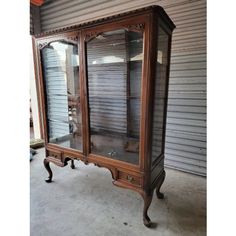 an antique china cabinet with glass doors and wood trimmings on the top, in front of a garage door