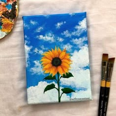 a sunflower painted on a canvas next to some paintbrushes