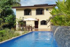 an empty swimming pool in front of a house with palm trees and plants around it