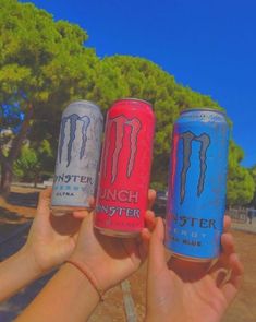 three cans of monster energy drink being held by two hands