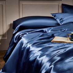 a blue satin bed spread with two coffee mugs on it and an open book