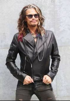 a man with long hair and sunglasses standing in front of a wall wearing a black leather jacket