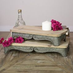 two wooden trays with candles and flowers on them sitting on a wood floor next to a bottle of water